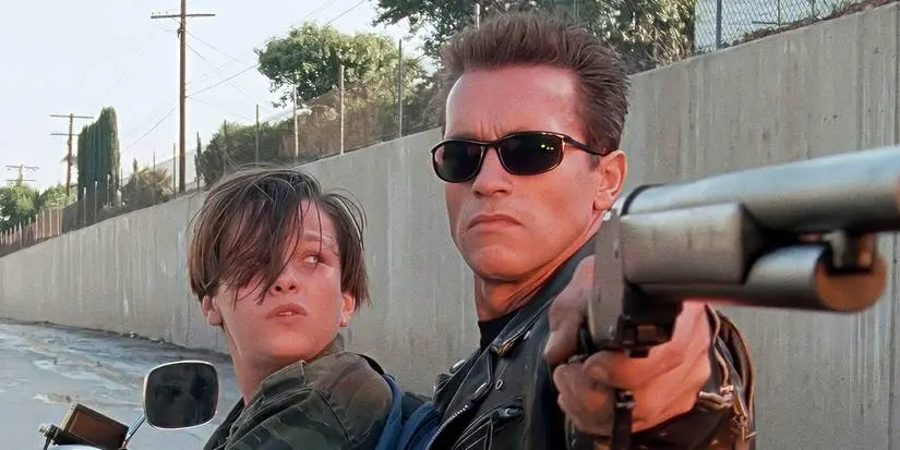 The T-800 aiming a rifle while John Connor sits in front of him in Terminator 2: Judgment Day