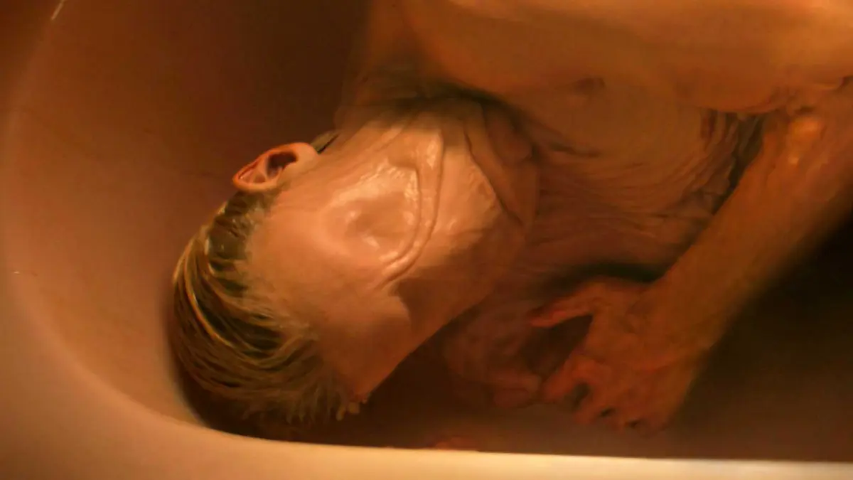 Tom Rhys Harries as Matt Hagen lying in a tub with his skin smoothed out in Clayface