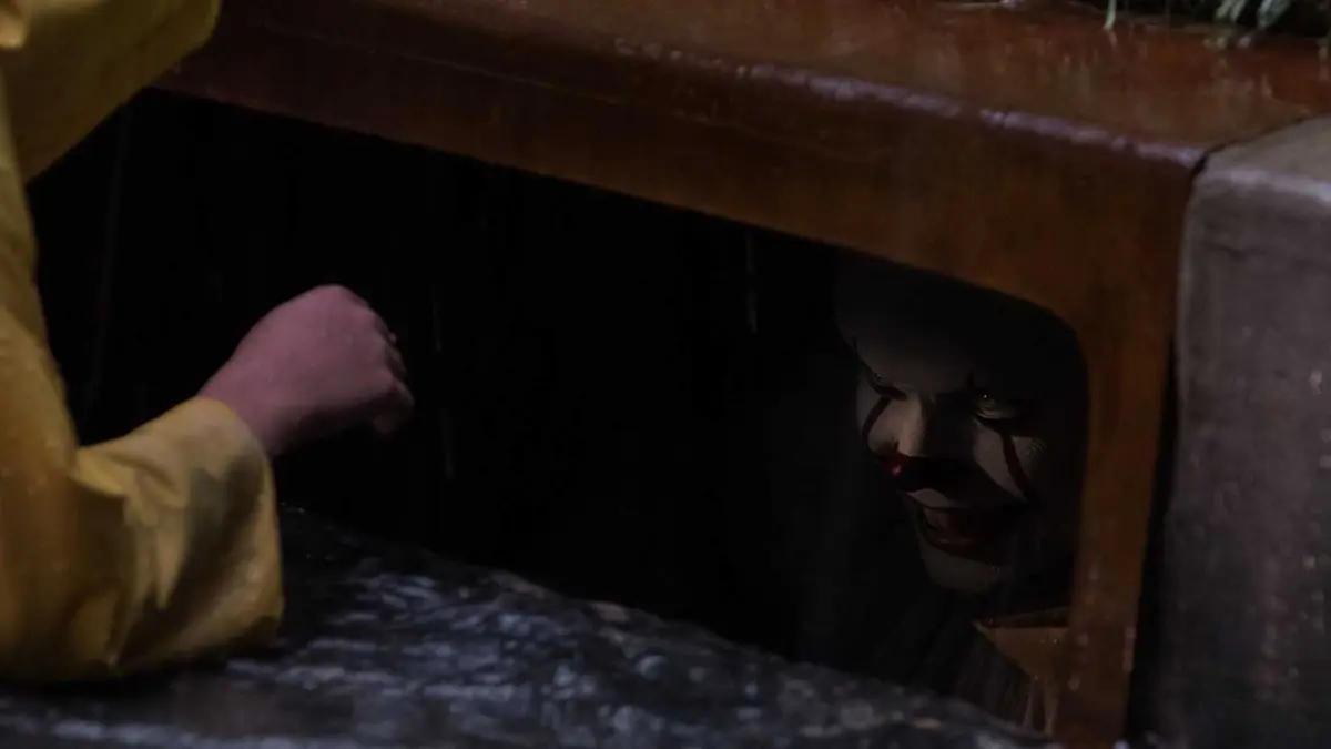Georgie (Jackson Robert Scott) reaching into the sewer while Pennywise (Bill Skarsgård) watches and smiles in It.