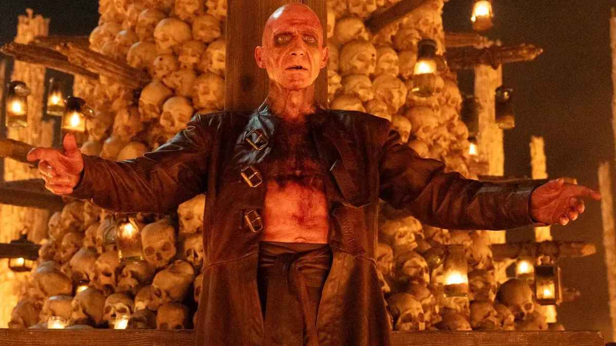 Ralph Fiennes as Dr Kelson spreading his arms in front of a skull tower in 28 Years Later The Bone Temple