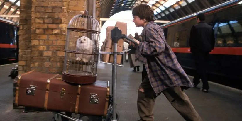 Harry (Daniel Radcliffe) pushes his trunk with Hedwig in her cage at Kings Cross Station in Harry Potter and the Sorceror's Stone