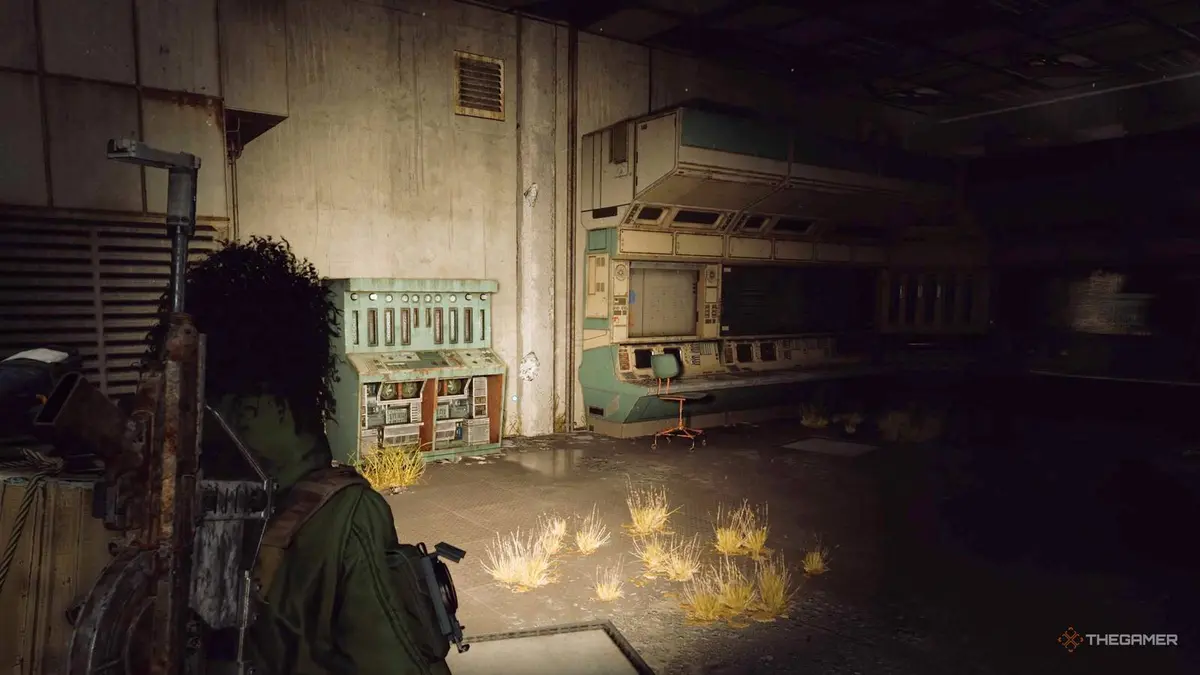 Player raider approaching a series of consoles inside a building with their flashlight on in Arc Raiders.
