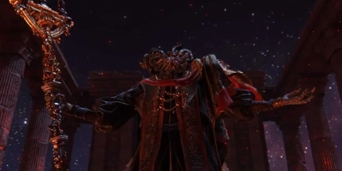 Mohg, Lord of Blood in Elden Ring. He holds his staff in his right hand while also lifting his left hand. His face is filled with horns which make it near undescribably. He stands in a dark arena with