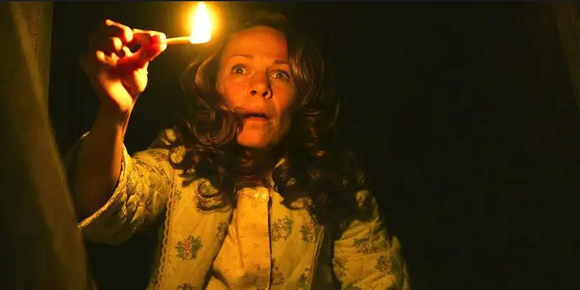 Lili Taylor&nbsp;as Carolyn Perron looks scared, holding a single match in a dark place in 'The Conjuring'