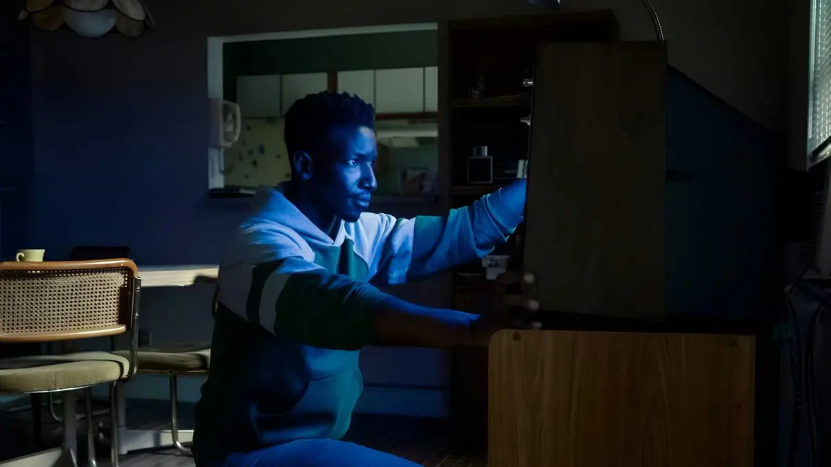 Mamoudou Athie‘s Dan Turner sitting in front of a TV’s blue screen in Archive 81