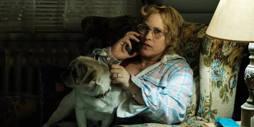 Patricia Arquette sits in a chair talking on the phone with a dog on her lap in Escape at Dannemora.