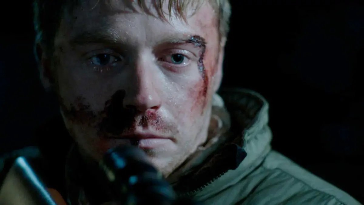 Jack Lowden as Vaughn bleed and holding a rifle in Calibre
