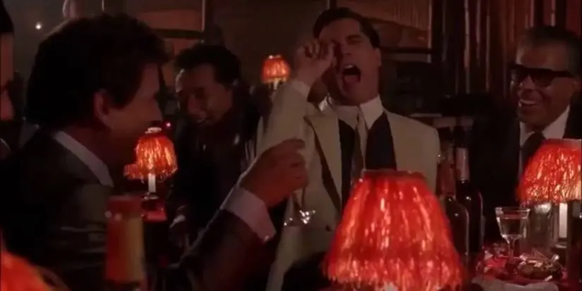 Joe Pesci and Ray Liotta laughing at a table in the "Funny how" scene in Goodfellas