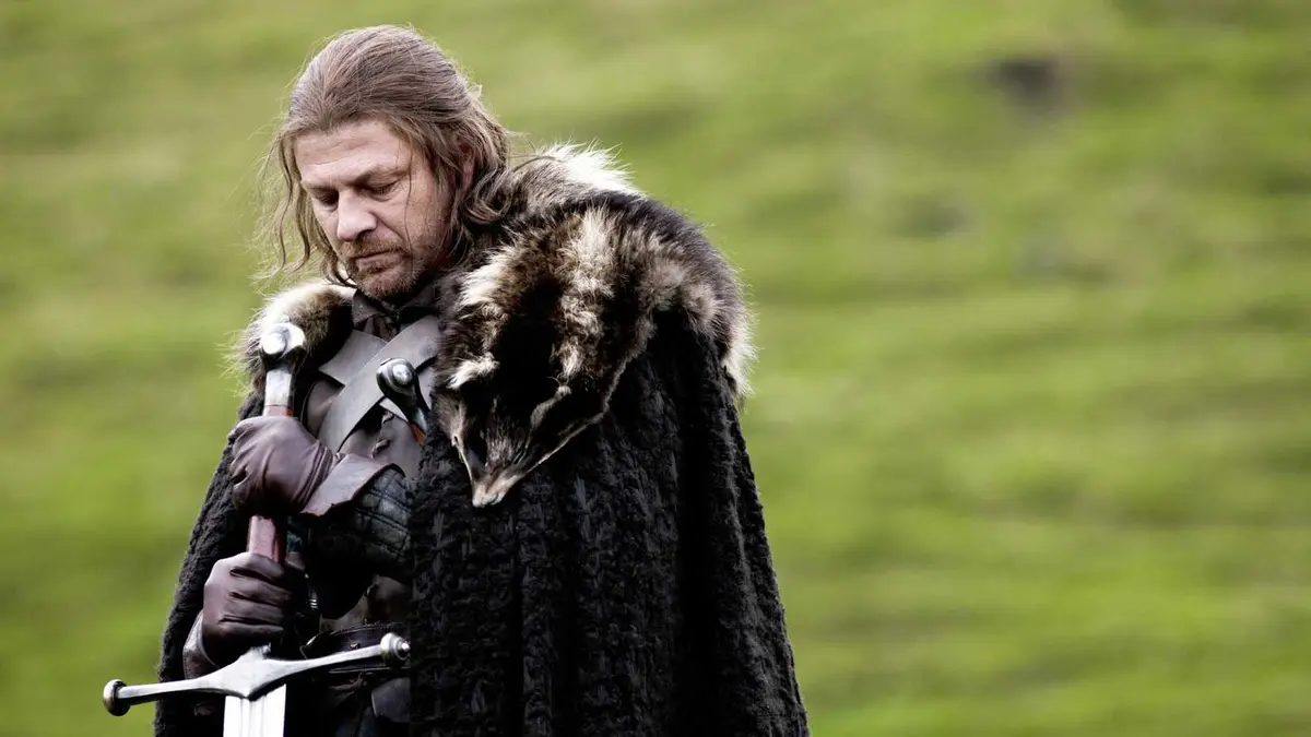 Sean Bean as Ned Stark holding a sword and looking down in Game of Thrones season 1, episode 1