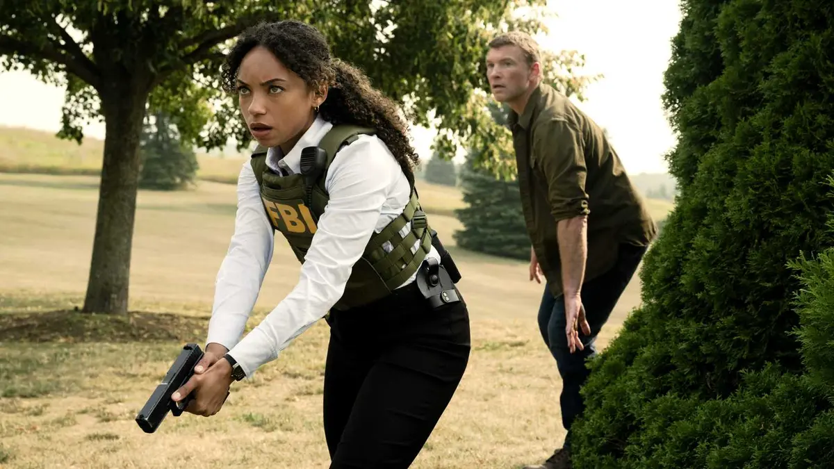 Logan Browning's Sarah holding a gun and walking crouched with Sam Worthington's David behind her in I Will Find You
