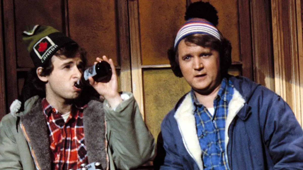 Two Canadian men wearing winter hats, plaid shirts, and jackets drinking beer