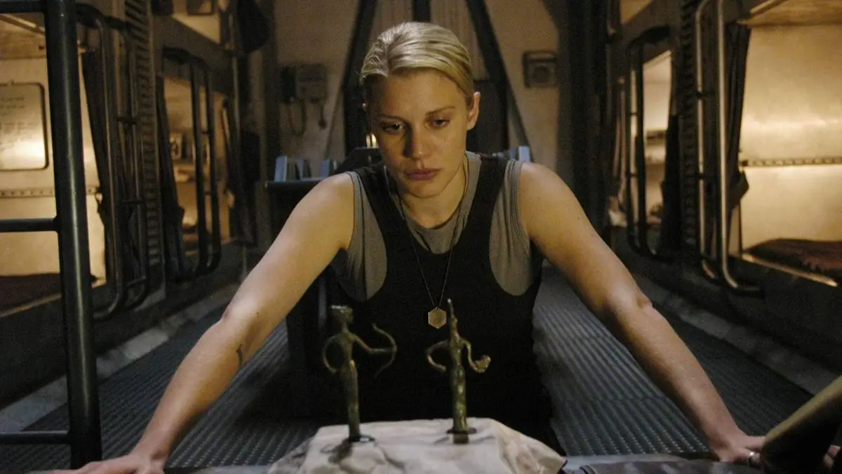 Kara leaning against a table with figures on it in Battlestar Galactica