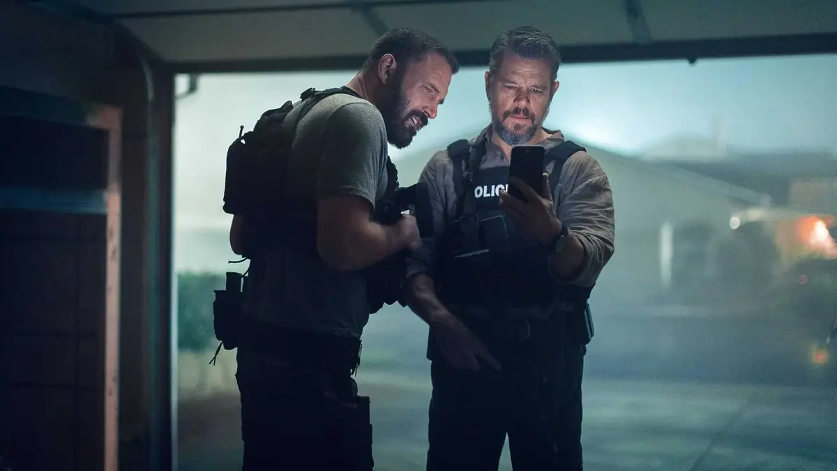 Matt Damon and Ben Affleck looking at a phone while standing in a garage in The Rip
