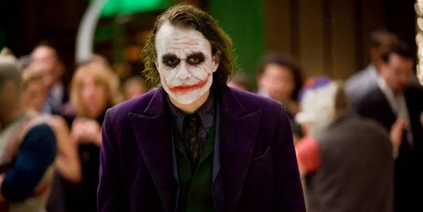 Heath Ledger's Joker, wearing his purple jacket and make-up, walks through a party in The Dark Knight