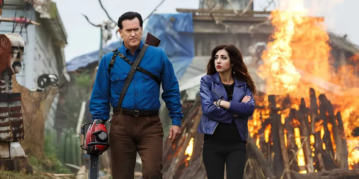 Ash (Bruce Campbell) and Kelly (Dana DeLorenzo) walk away from a burning building in Ash vs Evil Dead.