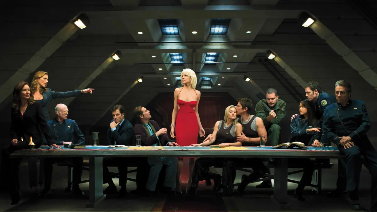 The main cast of Battlestar Galactica sitting at a table with Number 6 in the middle