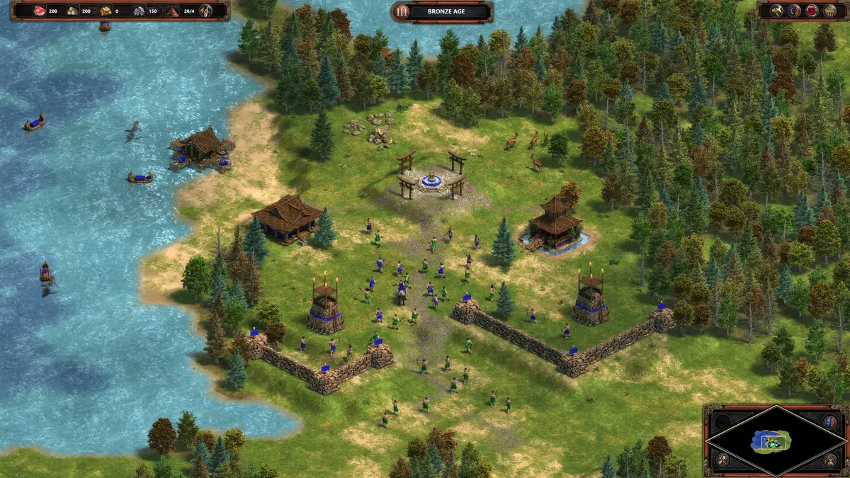 Blue and green infantry clash near stone walls and watchtowers in a forested coastal settlement in Age of Empires Definitive Edition