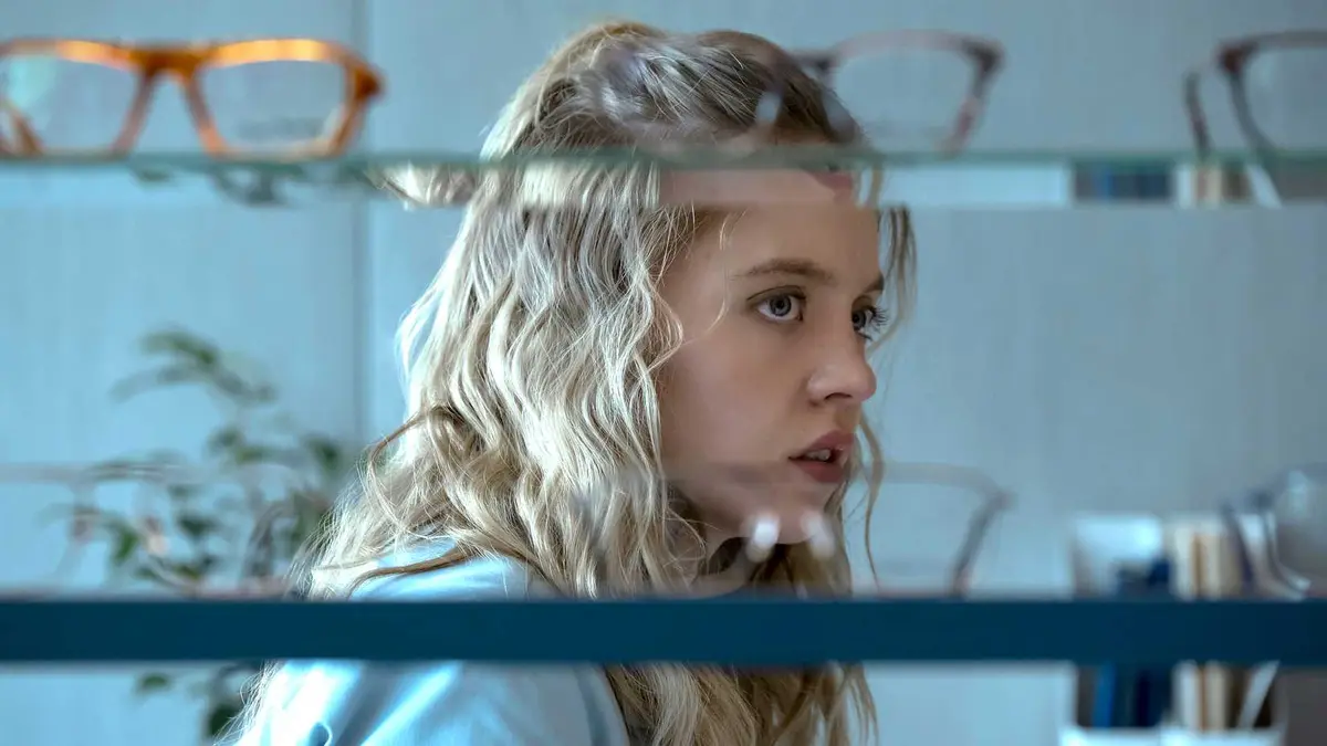 Sydney Sweeney's Pippa looking worried behind shelves with glasses on it in The Voyeurs