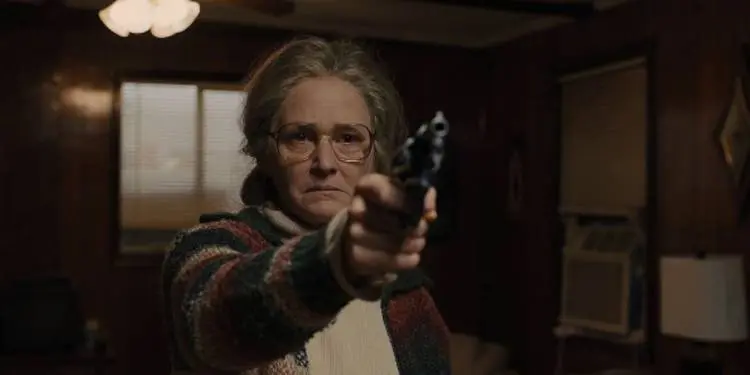 Melissa Leo as Holly aiming a gun in a wood-paneled room in Prisoners