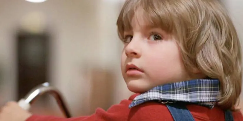 Danny Torrance looks behind him while riding his tricycle in The Shining