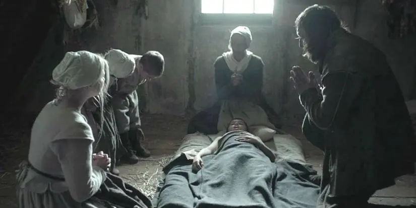 Family members praying around each other in The Witch.