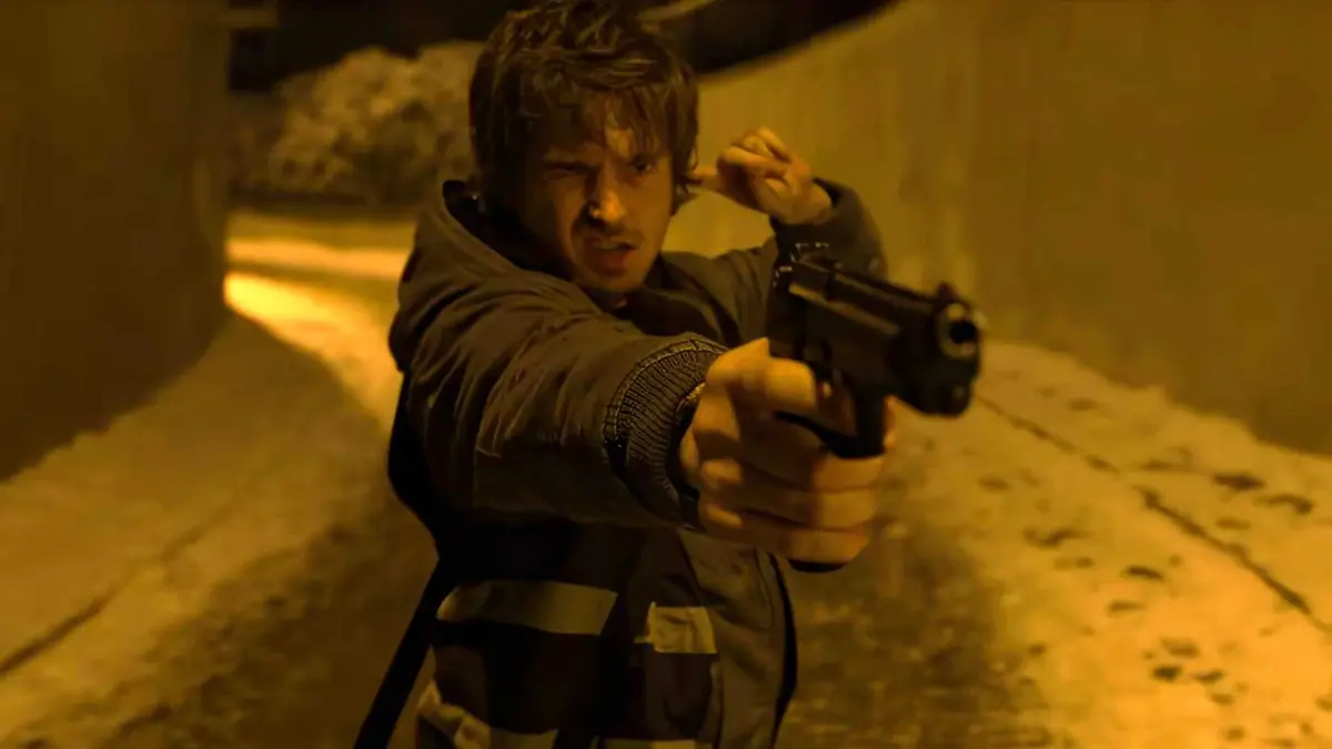 Austin Abrams' Bryan aiming a gun and putting a finger in his ear in Resident Evil