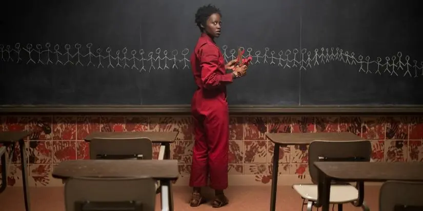 Lupita Nyong'o looking back infront of a blackboard in a dark classroom in "Us"