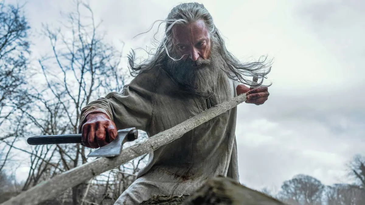 Hugh Jackman's Robin aggressively shaving a tree branch with an axe in The Death of Robin Hood