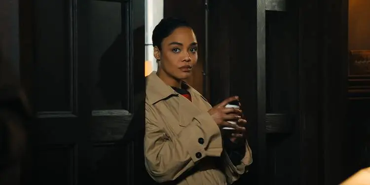 Tessa Thompson in a trench coat standing in a doorway in His & Hers.