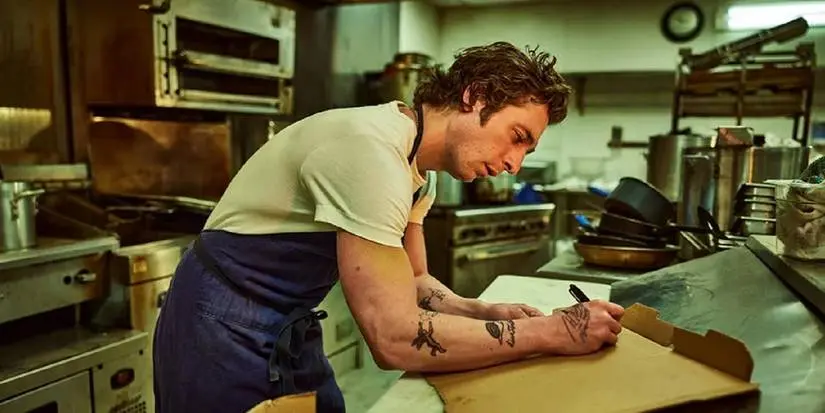 Jeremy Allen White as Carmy writing on a pizza box in The Bear