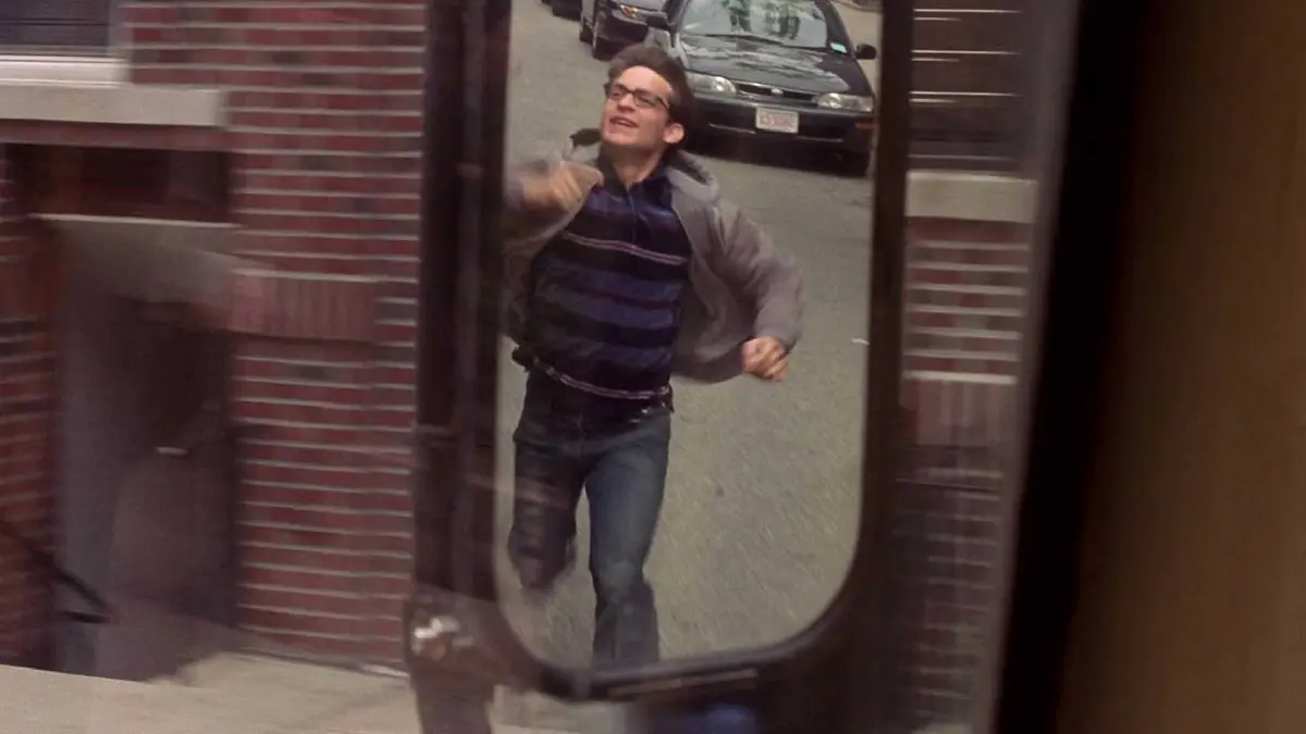 Tobey Maguire as Peter Parker running alongside a bus and being reflected in the mirror in Spider-Man (2002)