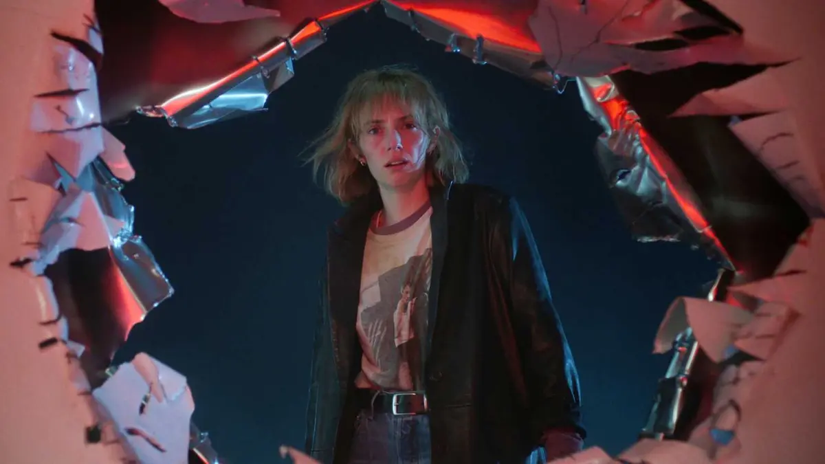 Maya Hawke's Robin stares through a hole in a metal wall in Stranger Things season 5