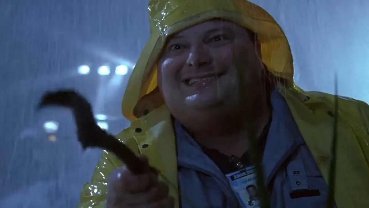 Dennis Nedry holding a stick trying to play with a dilophosaurus in Jurassic Park