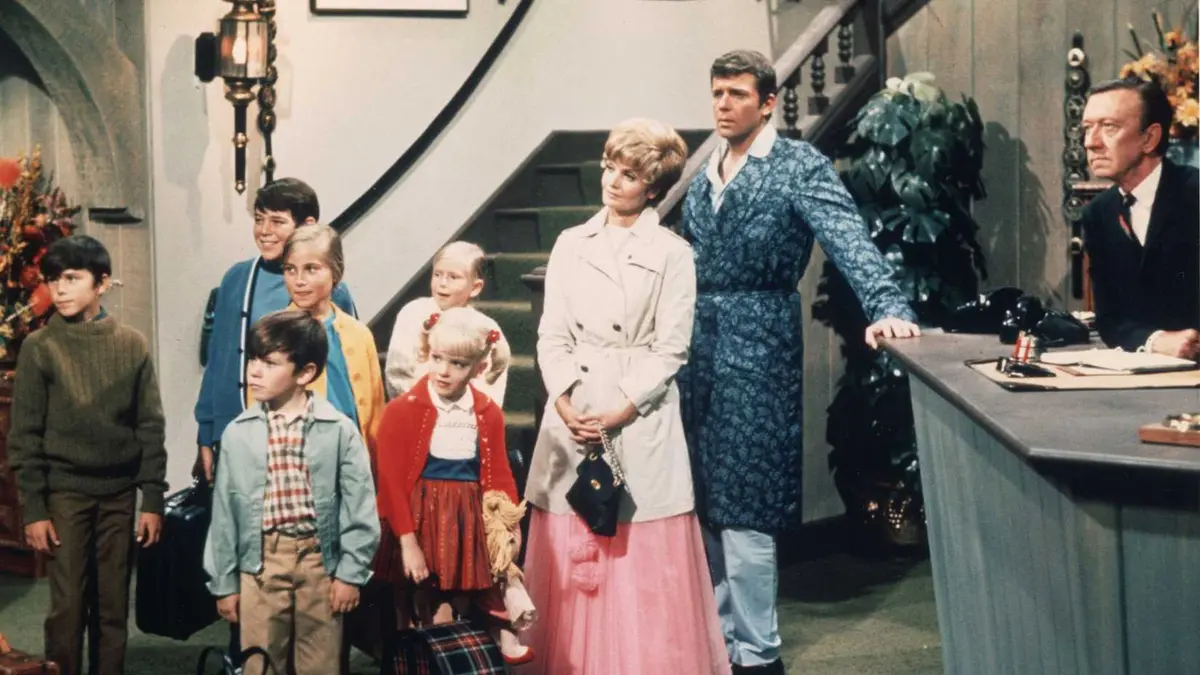 An adult male, an adult woman, and a bunch of children dressed in 70s clothing