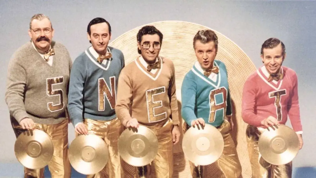 Five white men dressed like they're from the 1950s hold golden records and wear sweaters that spell out "5 NEAT"
