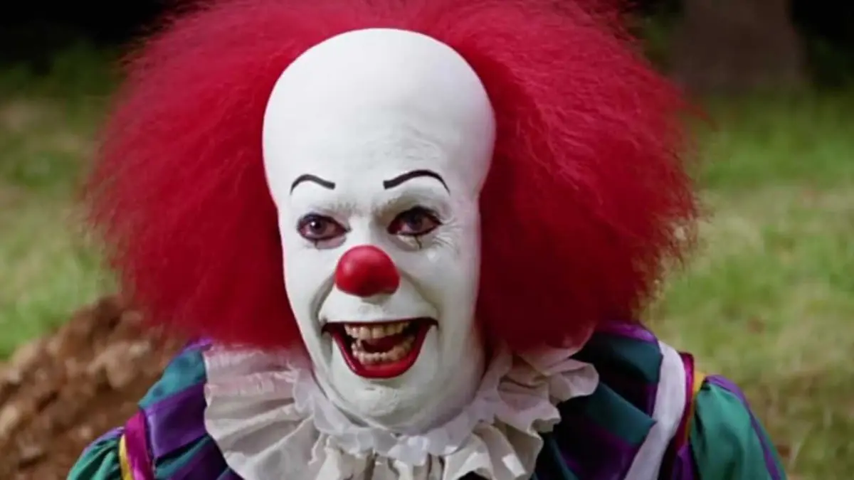 Tim Curry as Pennywise smiling in It 1990 miniseries
