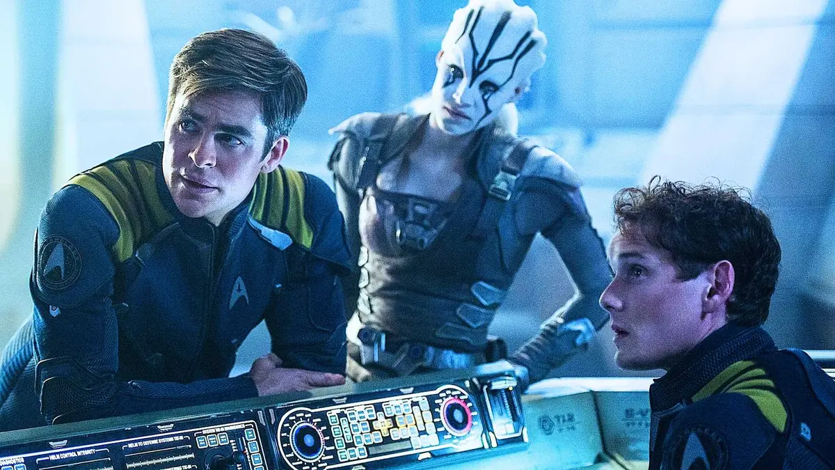 Captain Kirk and Pavel Chekov leaning on a console in blue uniforms with Jaylah, a white-skinned alien, from Star Trek Beyond