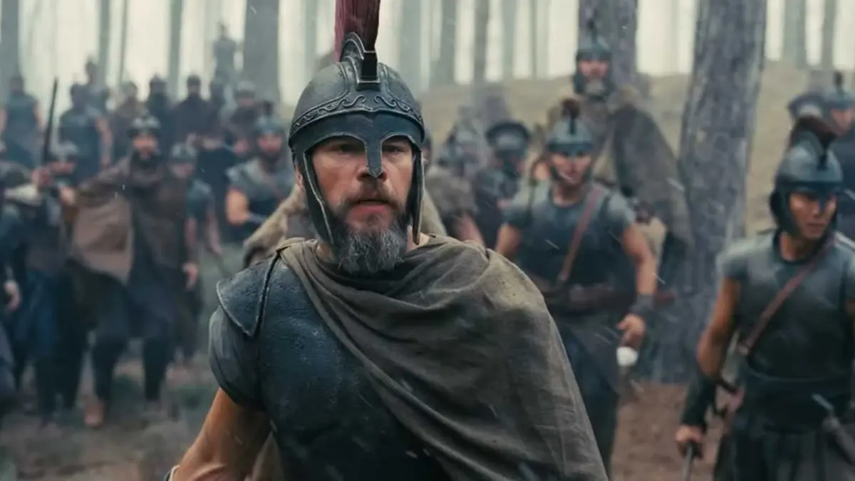 Odysseus stands in front of an army of armored men in the rain.