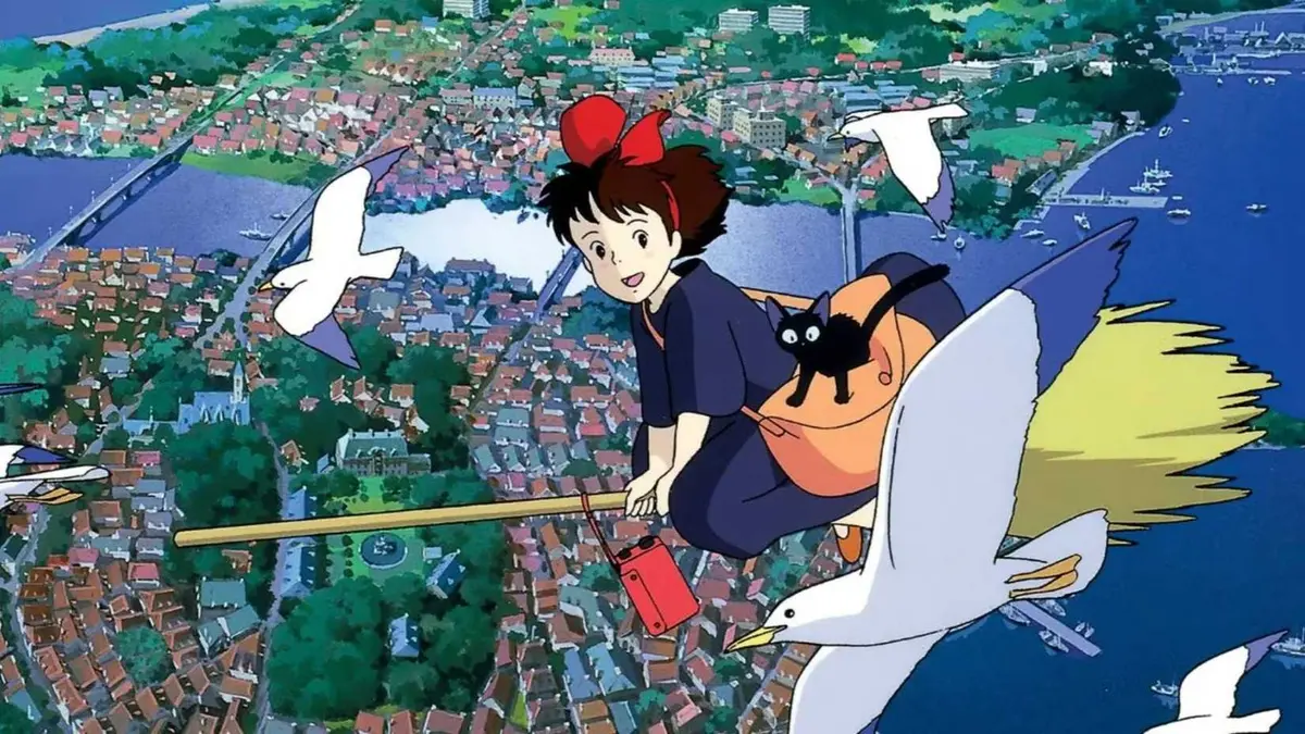 Kiki rides on her broom while Jiji sits on her bag beside her as they fly over the city in Studio Ghibli's Kiki's Delivery Service