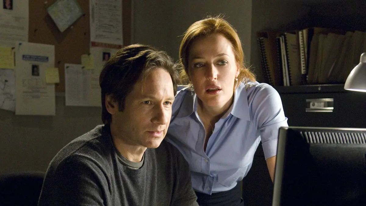 Gillian Anderson’s Dana Scully and David Duchovny’s Fox Mulder looking at a computer screen in The X-Files