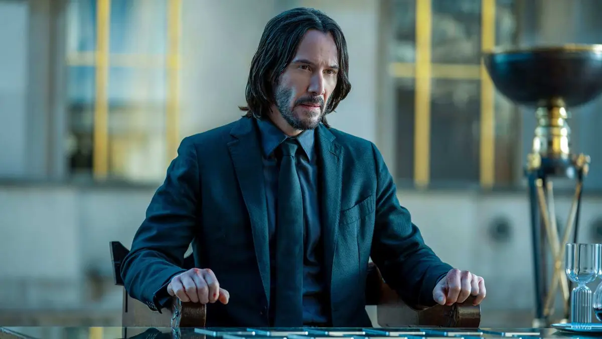 Keanu Reeves as John Wick sitting in a chair at a desk in John Wick: Chapter 4.
