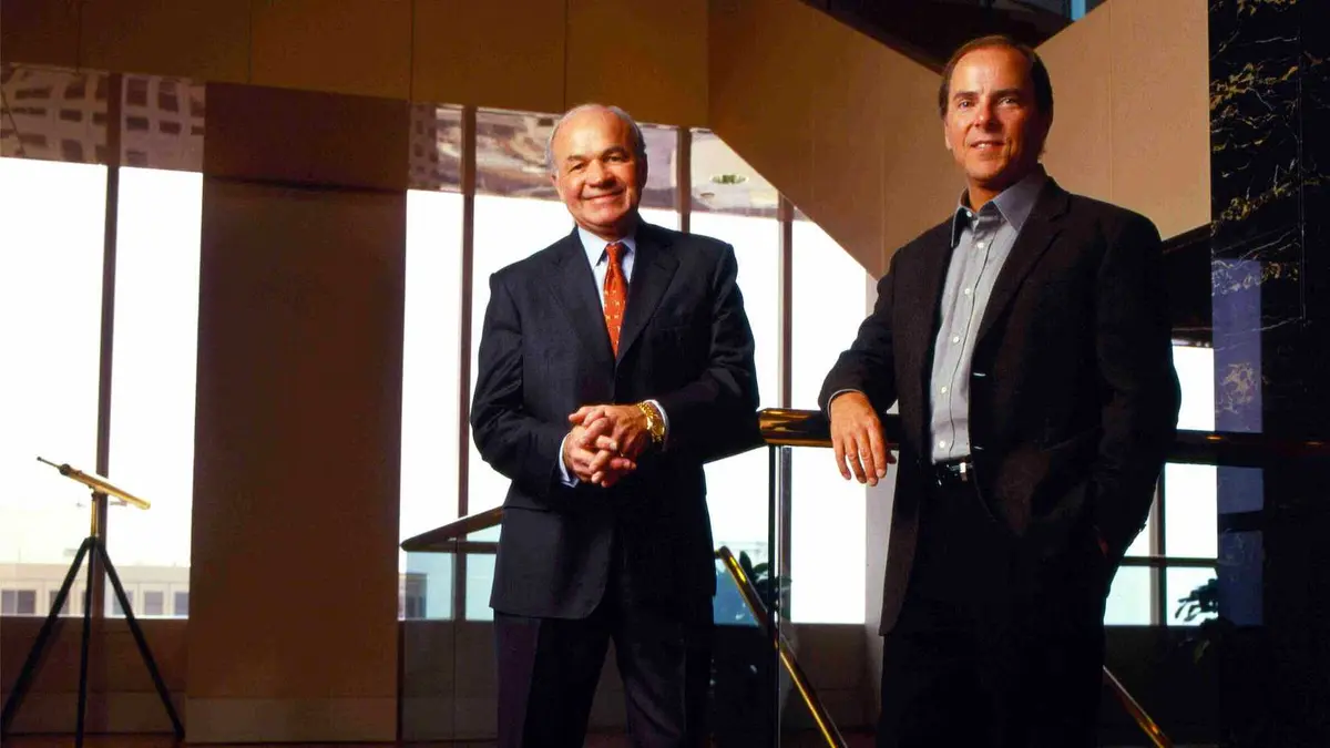 Two men in businesswear smile at a camera.
