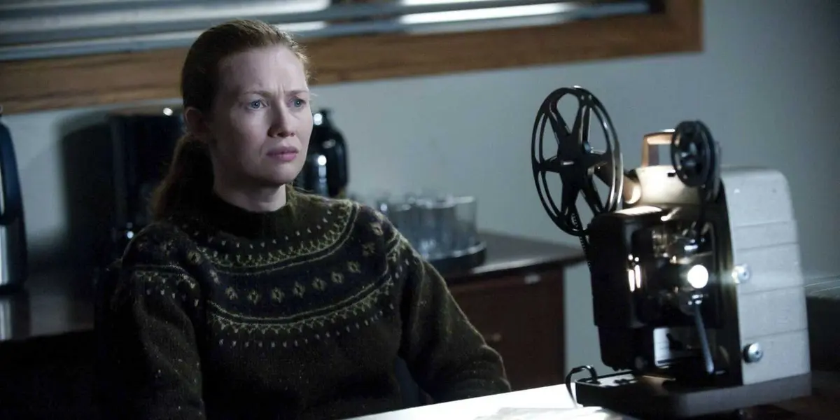 Mireille Enos as Sarah Linden sits in a chair and stares ahead at a projection in The Killing.