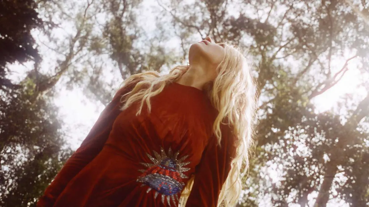 Prairie wearing a red dress and looking up at the trees in The OA