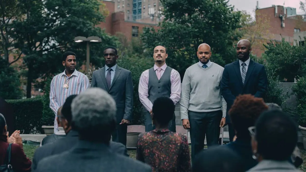 Five men stand on a stage looking out at a crowd in Netflix's When They See Us