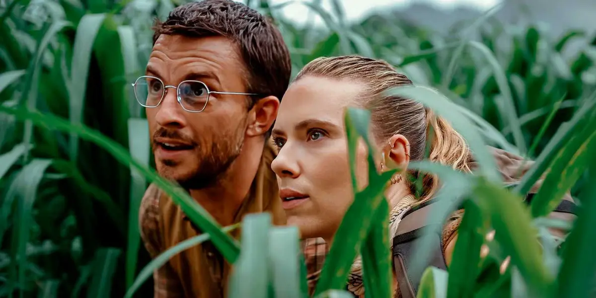 Scarlett Johansson and Jonathan Bailey kneeling in tall grass in Jurassic World Rebirth.