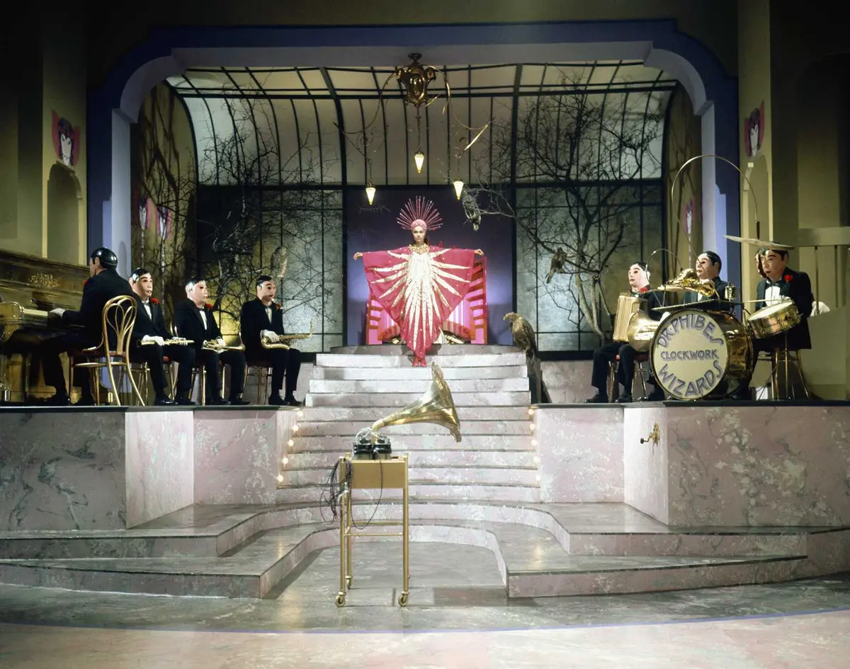A woman in a red sun peacock dress stands in the middle of a clockwork band