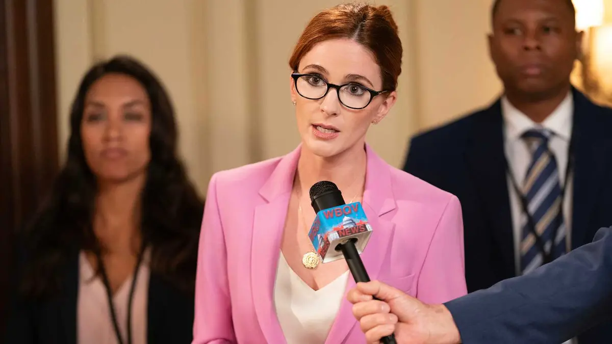 Stephanie Koenig in a pink suit speaking into a mic in Mid Century Modern